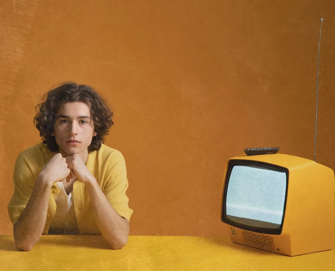 Young man seated beside a vintage yellow television